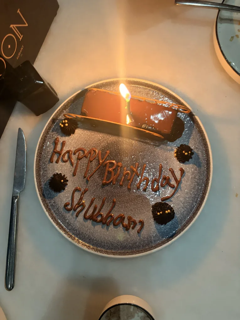A birthday dessert plate — Happy Birthday piped in chocolate around a lit candle, the Moon box on the marble beside it.
