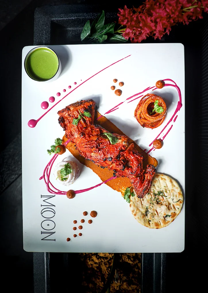 Tandoori chicken plated on the Moon board — mint chutney, pink swirls, garlic naan.