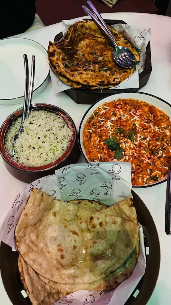 Dinner for the table — butter chicken, jeera rice and breads on Moon-printed paper.