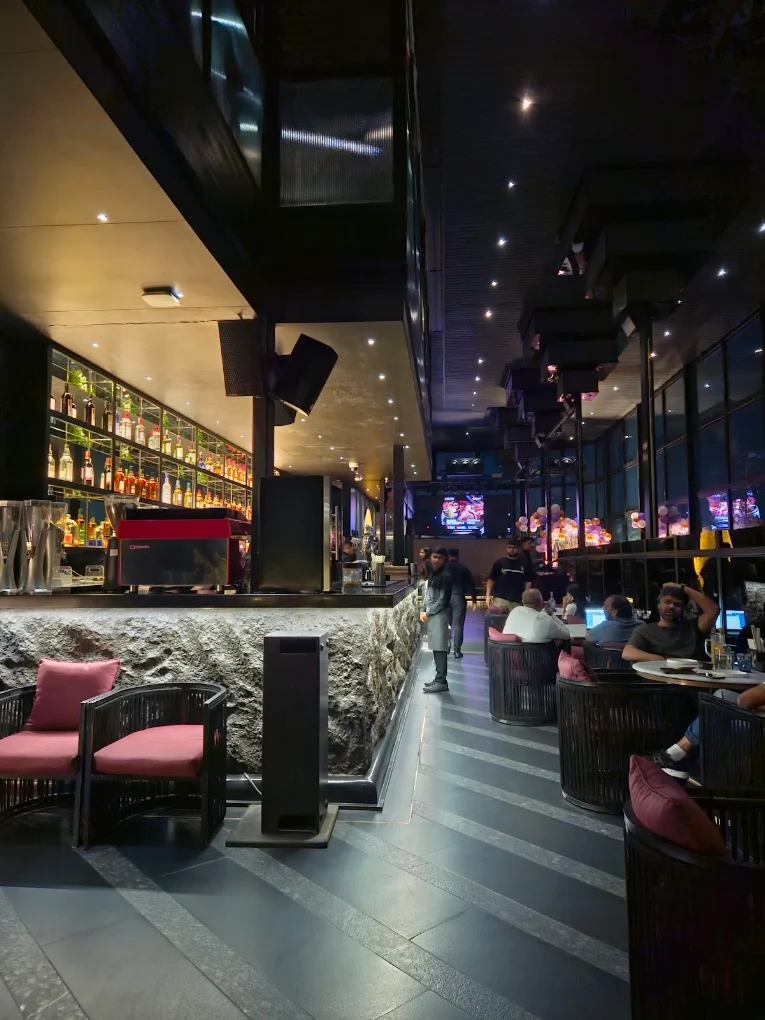 The floor at Moon mid-evening — the stone bar counter, the lit bottle wall and rose-pink chairs.