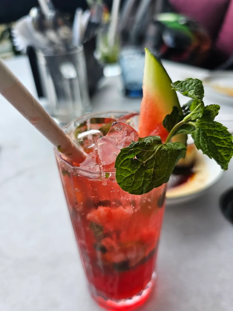 A watermelon mojito close up — ice, mint and a wedge of melon on the rim.